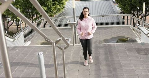 Young woman jogging up urban stairway wearing pink hoodie and wrist fitness tracker