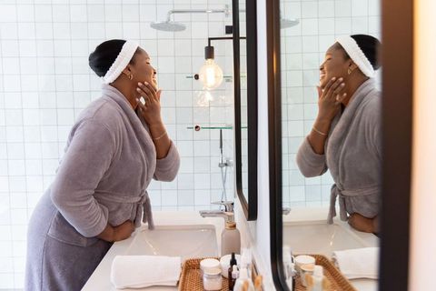 African american woman performing morning skincare routine at mirror in modern bathroom