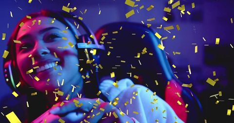Female gamer celebrating victory wearing headset-mic with gold confetti and neon rgb lights