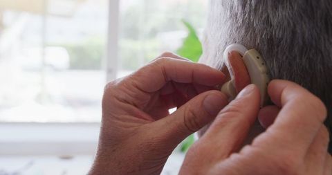Doctor adjusting hearing aid on senior patient in medical facility