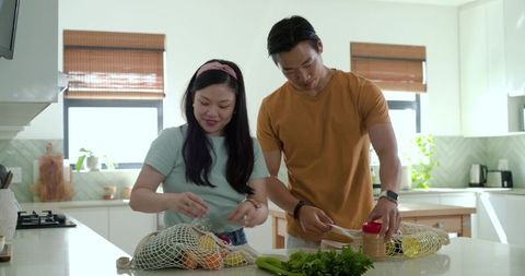 Couple unpacking groceries at bright kitchen island with mesh produce bags and herbs