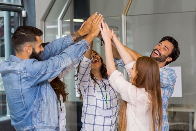 Group of diverse business professionals celebrating success with a high five in a modern office. Ideal for illustrating concepts of teamwork, collaboration, corporate culture, motivation, and workplace unity. Suitable for use in business presentations, corporate websites, team-building materials, and motivational content.