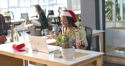 African american woman wearing santa hat leading virtual holiday meeting in modern office