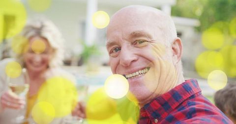 Smiling senior man wearing red-blue plaid shirt at sunlit backyard poolside gathering