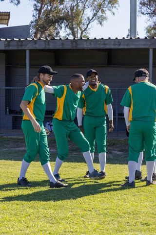 Baseball teammates celebrating and laughing on field before game wearing green uniforms