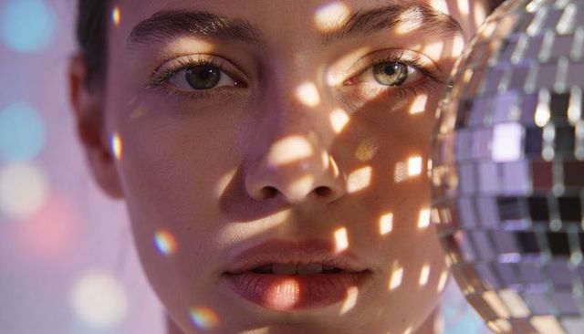 Gazing woman basking in disco ball reflections and prism light patterns closeup portrait