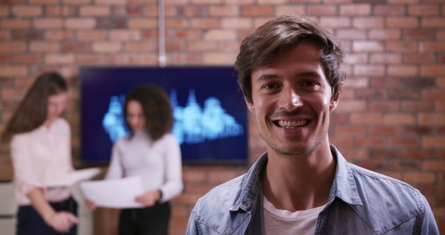 Smiling Man in Casual Office Setting with Colleagues Working in Background - Download Free Stock Images Pikwizard.com