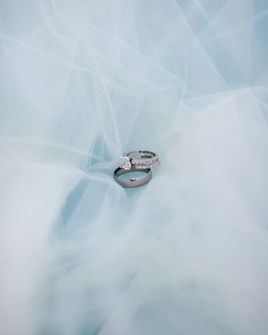 An elegant set of wedding rings, including a diamond engagement ring, placed atop a delicate soft blue veil background. Ideal for wedding invitations, romantic concepts, or anniversary cards, this image captures the timeless beauty of matrimonial symbolism and style.