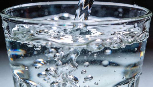 Pouring clear water into glass with rising bubbles close-up macro transparent motion