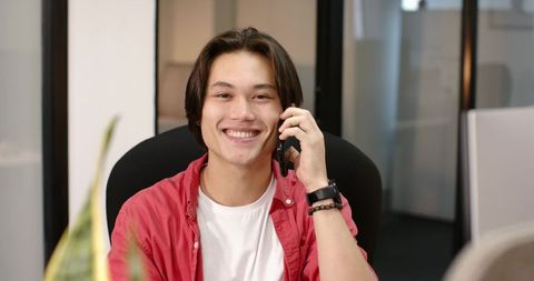 Asian professional joyfully talking on smartphone in modern office