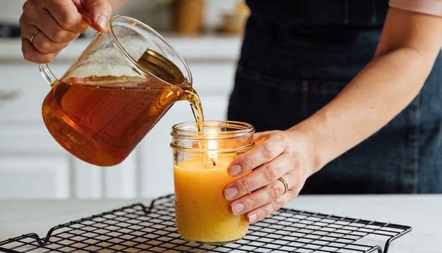 Pouring honey-colored wax into mason jar for handmade candle making