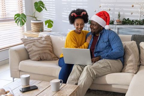 African american couple celebrating christmas at home using laptop on cozy sunlit sofa