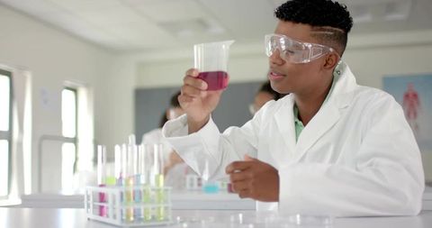 Teen scientist examining purple solution in school lab wearing protective goggles