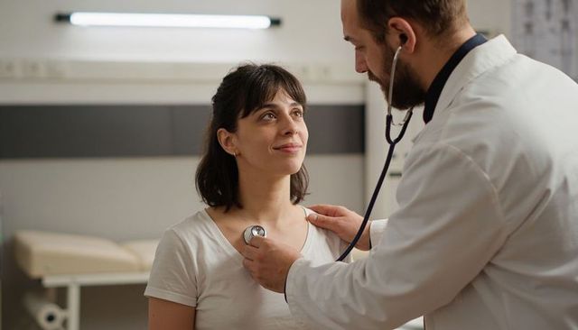 Male physician auscultating female patient with stethoscope in clinical consultation