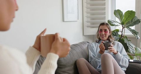 Friends Enjoying Cozy Skincare Tea Time on Sofa with Under-Eye Patches