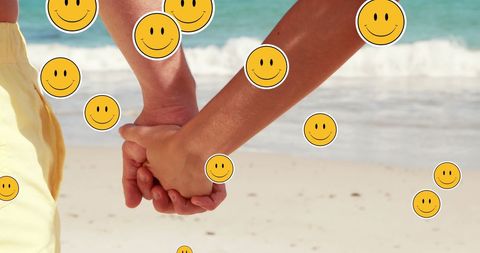 Couple holding hands on beach with smiley emojis overlay