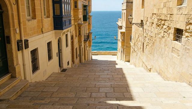 Sunlit limestone staircase descending to mediterranean sea through historic coastal alley