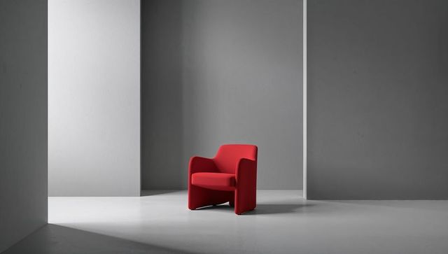 Red modern armchair in minimalist grey space with strong directional light and shadow