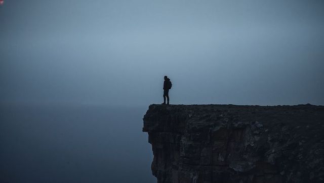 Solitary hiker standing on foggy sea cliff gazing into misty horizon
