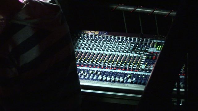 Indoor scene features a close-up of an audio mixing console in low light, highlighting knobs and controls. Useful for visuals in nightlife events, professional audio engineering, music production, and concert settings.