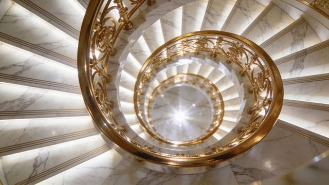 Spiraling white marble staircase with ornate gilded banister and radiant central light
