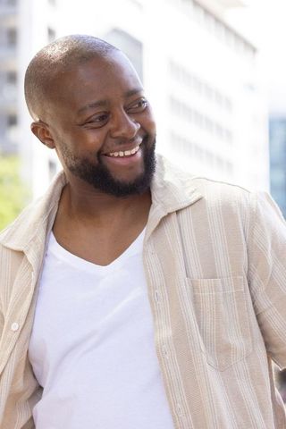 African man smiling and glancing sideways in beige striped overshirt and white v-neck