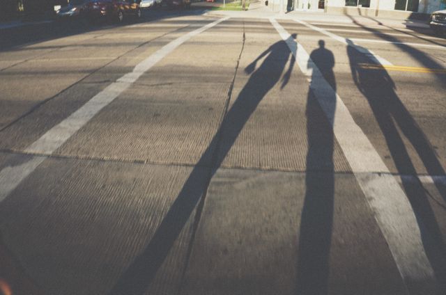 Shadows of people walking across an urban street during sunset create long, dramatic silhouettes. Suitable for illustrations or concepts related to commuting, city life, sunset, and the passing of time, as well as creating a sense of mystery or narrative in creative projects.