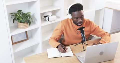 African American Podcaster Recording and Taking Notes with Microphone Laptop in Bright Home Office