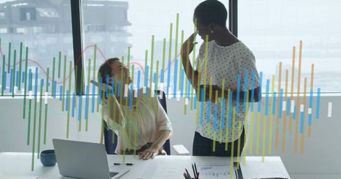 Businesswomen analyzing financial charts and data at bright office desk with laptop