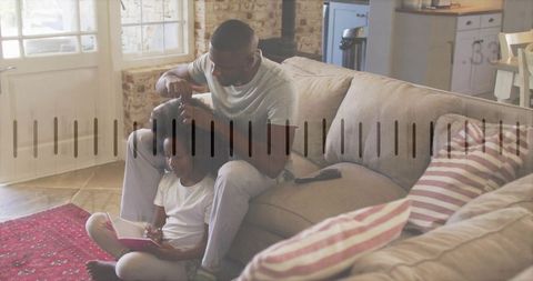 Dad brushing child hair on couch while child reading notebook cozy home bonding moment