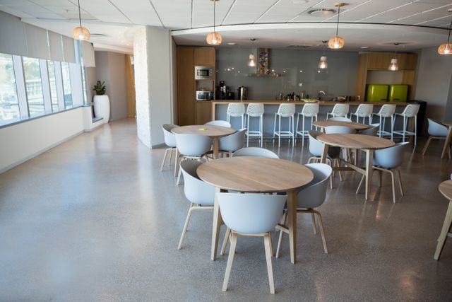 Modern office cafeteria featuring empty tables and chairs, ideal for illustrating corporate break areas or workplace environments. The clean and contemporary design makes it suitable for use in articles about office culture, workplace amenities, or interior design.