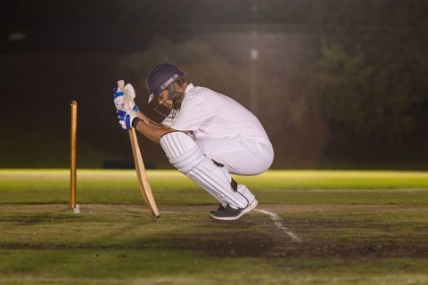 Cricketer squatting in batting crease at night under floodlights holding bat