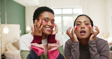 Diverse friends applying vegan under-eye masks in cozy bedroom