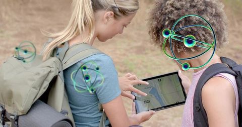 Teen hikers navigating trail with tablet, exploring map with AR overlays and backpacks