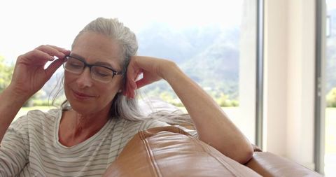 Serene Mature Woman with Gray Hair Relaxing on Sofa by Window