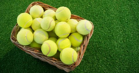 Pile of bright yellow tennis balls in wicker basket on grass