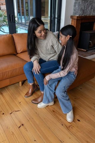 Asian mother and daughter sharing cozy conversation on tan leather sofa in living room