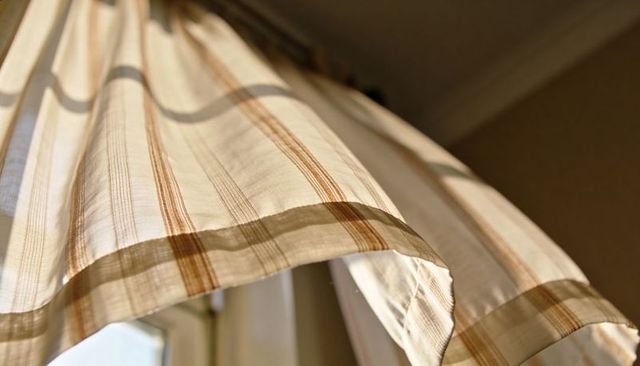 Sunlit striped curtain panel filtering warm light hem and pleats close-up for interiors