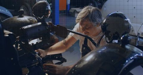 Mature mechanic repairing vintage motorcycle engine in garage workshop with chrome details