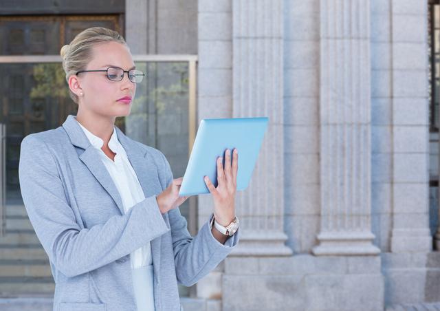 Businesswoman in formal attire holding a tablet and working outside an office building. Ideal for use in articles about business, corporate culture, women in leadership, and technology in the workplace.