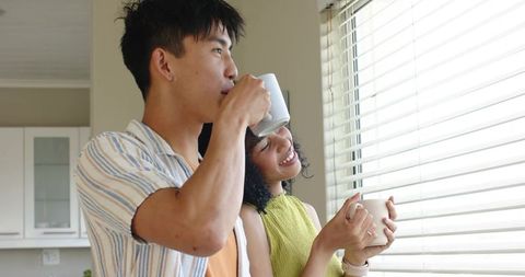 Sunlit African American woman and Asian man enjoying morning coffee in cozy kitchen