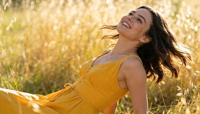 Joyful woman reclining in sunlit meadow wearing mustard dress during golden hour breeze