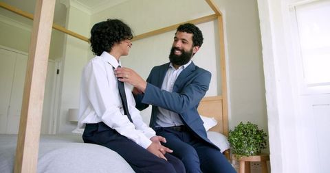 Father adjusting son's tie sitting on bed sharing moment
