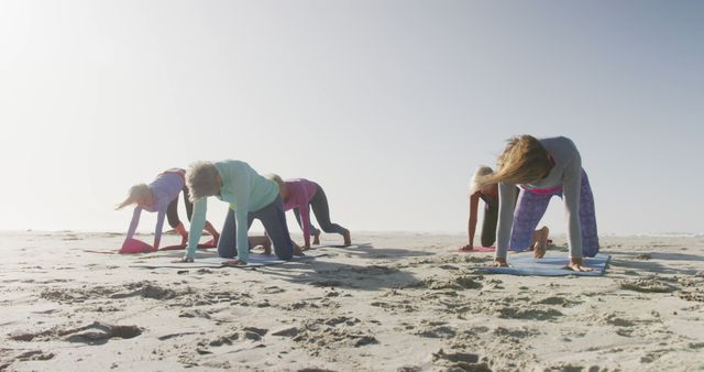 A group of women participating in a yoga class on a sandy beach, practicing various poses. This can be used in articles or promotions focused on fitness, wellness activities, outdoor exercising, and healthy lifestyle events. It highlights harmony with nature and the communal aspect of yoga practice.