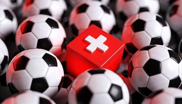 Red medical cube standing out among soccer balls conveying sports injury concept