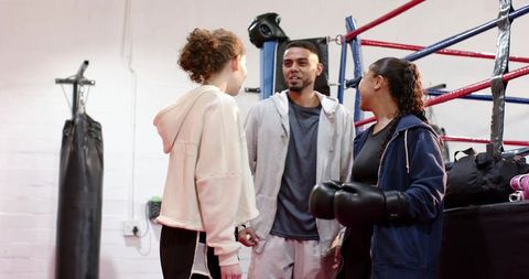 Female boxer shaking hands with trainer and teen trainee in boxing gym