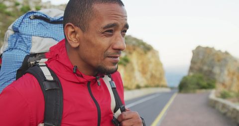 Determined man backpacking along coastal road at sunrise