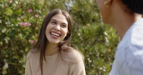 Laughing young woman talking with friend in sunlit garden, candid friendship portrait