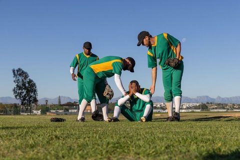 Baseball teammates consoling upset player on grass field demonstrating teamwork and support
