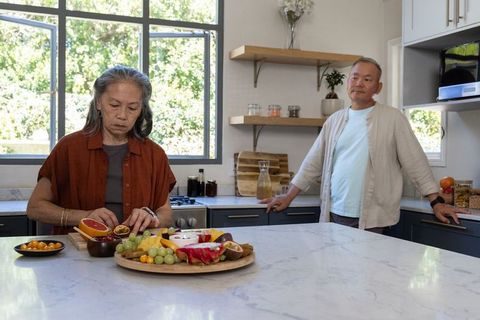 Mature diverse couple preparing fresh fruit on marble island in modern kitchen